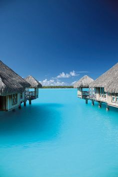 the water is very blue and there are overhanging huts on stilfes