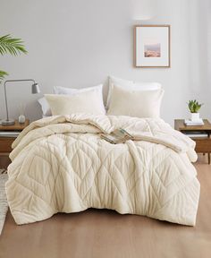 a bed with white comforter and pillows in a room next to a wooden table