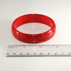 This is part of Chairish’s Costume Jewelry assortment.  Lipstick red Bakelite bangle bracelet with carving. We believe this piece dates to the 1930s. Unmarked. Measures about 7 1/2" inches in circumference inside and about 5/8" wide. Opening is 2 1/2" across. Red Retro Bangle Jewelry, Vintage Red Round Bangle, Red Carved Vintage Jewelry, Carved Red Vintage Jewelry, Vintage Red Adjustable Bangle, Bakelite Bangles, Lipstick Red, Bangle Bracelet, Costume Jewelry