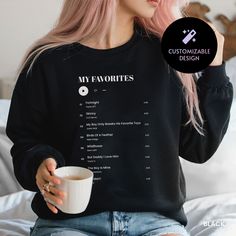 a woman with pink hair is holding a coffee cup and wearing a black sweatshirt that says my favorites