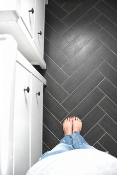 a person standing on the floor in front of a white cabinet and black tiled wall