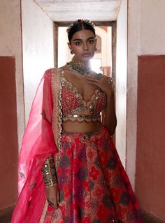 This exquisite banarasi lehenga, inspired by the elegance of jharokhas, is beautifully paired with a coral plunging V-neck sheeted blouse and a flowing organza dupatta. Delicately highlighted with cut mirrors and pearls, the ensemble radiates sophistication and charm. A stylish belt cinches the waist, enhancing the silhouette and completing this stunning look with a perfect blend of tradition and contemporary flair. Chanderi Lehenga, Banarasi Lehenga, Silk Lehenga, Organza Dupatta, Silk Blouse, Lehenga, Coral, Cute Outfits, V Neck