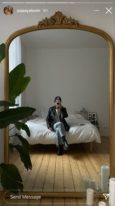 a man sitting on top of a bed in front of a large gold frame mirror