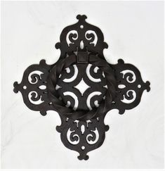 an ornate black iron door handle on a white wall with swirls and scrolls in the center