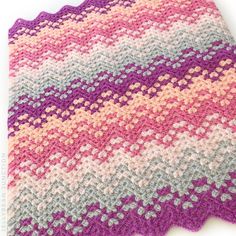 a crocheted blanket is laying on top of a white surface with pink, grey and yellow colors