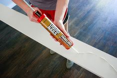 a woman holding a tube of glue on top of a wooden floor