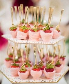 small desserts with strawberries and gold forks are arranged on a cake stand at a wedding reception