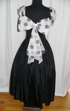 This is a wonderful party dress made in the 1980's that is style of the 1950's full skirt party dresses. The dress has a a deep V'd scoop neckline with an attached polka dot scarf of organza that follows the neckline through a loop at the front and then becomes the shoulder straps and end at the back with a huge bow and streamers. The material is most likely a polyester with a faille texture. It fits tightly through he dropped V waist line both at the front and back. The bodice is not lined but Retro Polka Dot Dress For Evening, Retro Polka Dot Evening Dress, Retro Polka Dot Dresses For Party, Vintage Bow Dress For Costume Party, 1950s Style Polka Dot Party Dresses, Polka Dot 1950s Style Party Dress, Vintage Party Dress With Bow, Vintage Style Black Party Dress, Retro Black Wedding Dress