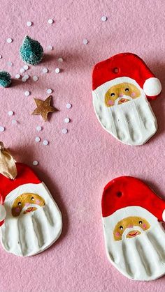 three santa claus ornaments on a pink surface with glitters around them and one is holding a star