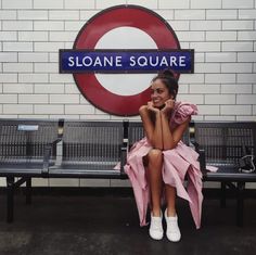 a woman sitting on top of a bench next to a train station sign with the name sloane square