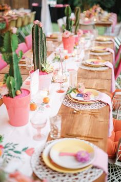 a long table with plates and cactus plants in pots on it's sides, along with other place settings