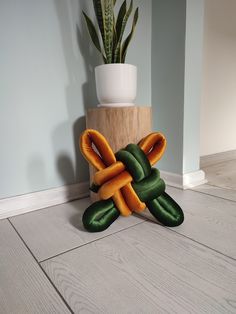 an orange and green knot sitting on the floor next to a potted plant