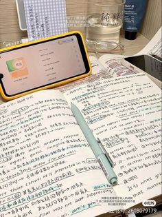 a cell phone sitting on top of an open book next to a pen and paper