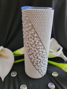 a white vase sitting on top of a black table next to flowers and pearls in front of it