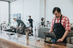 a man standing at a counter with an ipad in front of him and people working behind him