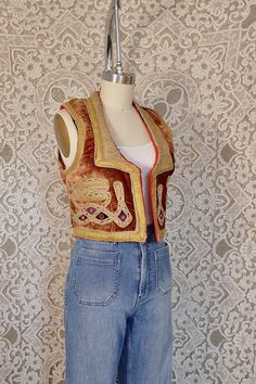 This sweet little vest is made from  rich brown velvet, with intricate dense embroidery and mirrorwork. It's a bohemian gem, and this piece is great layered over a jacket, blouse, or a simple t-shirt. This piece has no tags but would best fit a size extra small, see measurements for details. Measurements Shoulder: N/A Bust: 16.5" Sleeve" N/A Length: 16" Fitted Floral Embroidered Vest For Fall, Festive Bohemian Vest, Festive Bohemian Vest With Floral Embroidery, Bohemian Brown Vest Top, Bohemian Festival Vest With Floral Embroidery, Bohemian Vest Tops For Fall, Bohemian Festival Vest, Fitted Bohemian Vest For Festive Occasions, Bohemian Embroidered Festival Vest