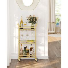 a gold bar cart with bottles and glasses on it in front of a white wall