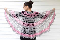 a woman wearing a pink and black crochet shawl with her arms wrapped around her shoulders