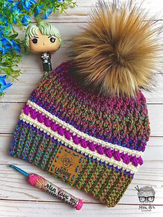 a knitted hat with a pom - pom sitting next to blue flowers