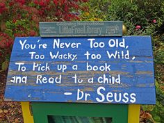 a blue sign with words written on it in front of some bushes and flowers,