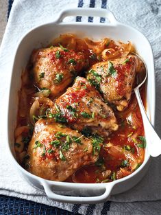 chicken with tomato sauce and onions in a white casserole dish on a blue towel