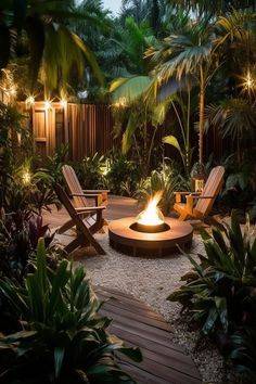 an outdoor fire pit surrounded by tropical plants and trees with lights on the sides, along with lawn chairs