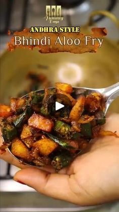 a person holding a spoon full of food in front of a pan with the words bhindi aloo fry on it