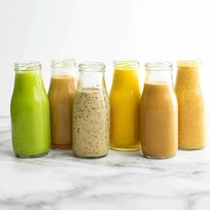 six different types of smoothies lined up in glass jars on a marble countertop