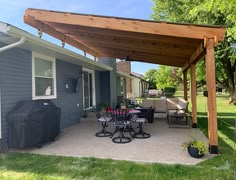 an outdoor patio with grill, table and chairs on the side of the house that is covered by a wooden pergoline