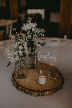 two vases filled with flowers on top of a wooden slice next to a candle