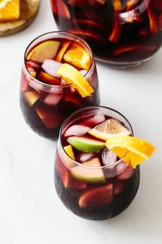 two glasses filled with fruit and ice on top of a white counter next to sliced oranges