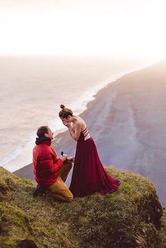 a man kneeling down next to a woman on top of a cliff near the ocean