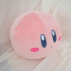 a pink stuffed animal with blue eyes laying on a white sheet