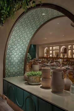 there are many vases and bowls on the counter in this room with green tiles