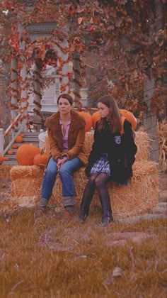 two women sitting on a hay bale with pumpkins in the background