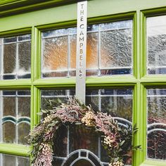 a green door with a wreath hanging on it's side next to a window