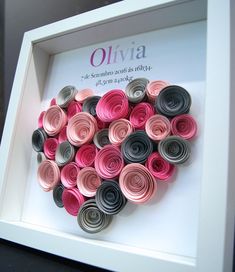 a white frame with pink and grey rolled paper flowers in it's center, on top of a black table