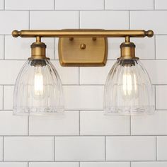 two clear glass lights are mounted on a brass wall light fixture over a white tiled wall