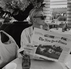 a woman sitting at a table reading the new york times