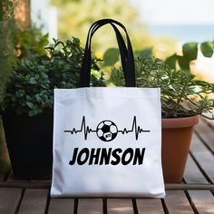 a white tote bag sitting on top of a wooden table next to potted plants