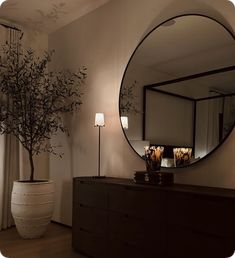 a large round mirror sitting on top of a wooden dresser next to a vase filled with flowers