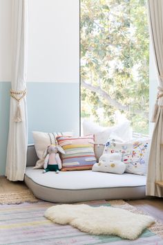 a bed with lots of pillows on top of it in front of a large window