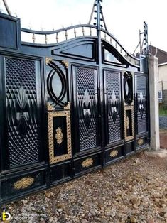 a black gate with gold designs on the top and bottom part, in front of a house