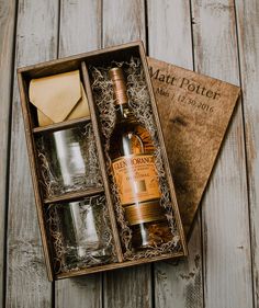 an open box with two glasses and a bottle in it sitting on a wooden table