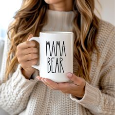 a woman holding a coffee mug with the words mama bear printed on it in black