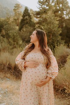 a pregnant woman standing in the grass with her hands on her stomach and looking off into the distance