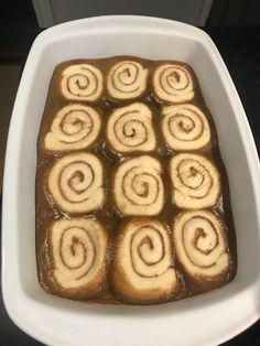 a white dish filled with cinnamon rolls sitting on top of a counter next to a stove