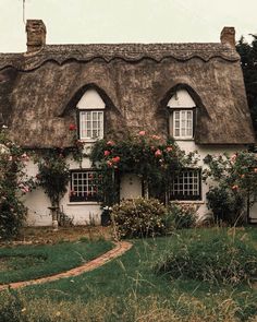 an old thatched roof house with roses growing on the windows and bushes in front