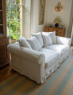 a white couch sitting in the middle of a living room next to a wooden dresser