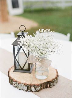 a vase filled with white flowers sitting on top of a wooden slice next to a lantern